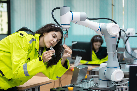Engaged young woman student engineer in teamwork, learning about robot technology with robotic arm. Future education for industry automation and modern programming for machinery