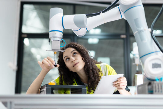 Female engineer closely inspecting and adjusting robotic arm components in high-tech industrial environment, symbolizing precision, innovation, smart automation.