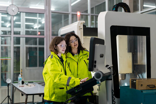 Team engineers wearing safety glasses operate CNC machine control panel in modern factory, showing precision manufacturing, automation, teamwork, quality control, production technology.