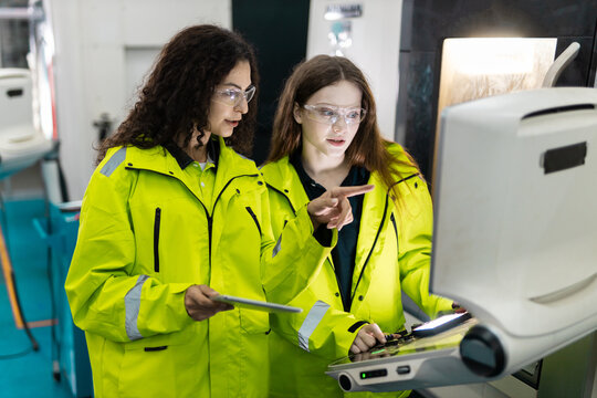 Team engineers wearing safety glasses operate CNC machine control panel in modern factory, showing precision manufacturing, automation, teamwork, quality control, production technology.