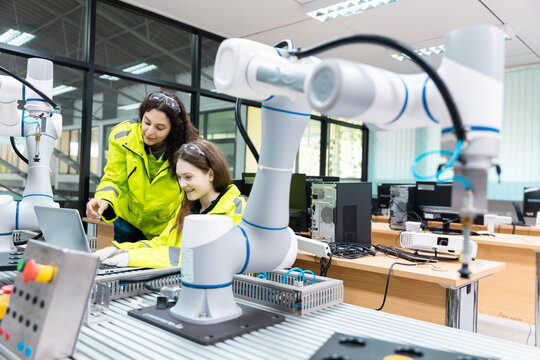 Engaged young woman student engineer in teamwork, learning about robot technology with robotic arm. Future education for industry automation and modern programming for machinery