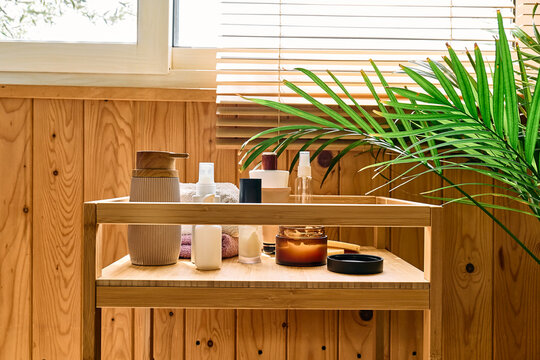 Skincare and beauty products, facial cream, towels and a houseplant arranged on a wooden tray in warm natural sunlight, representing personal care and a daily beauty routine.