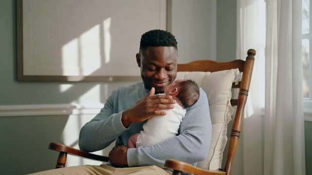 Cradling father soothing newborn after stirring, patting, rocking in rocker at home, blue top
