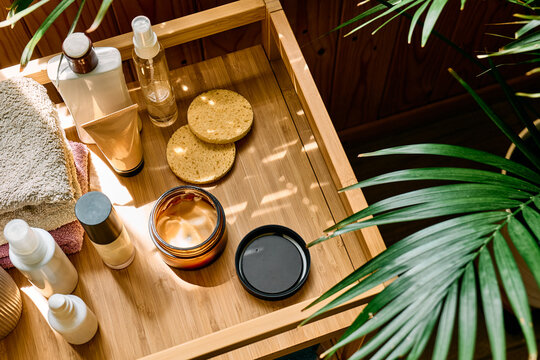 Skincare and beauty products, facial cream, towels and a houseplant arranged on a wooden tray in warm natural sunlight, representing personal care and a daily beauty routine.