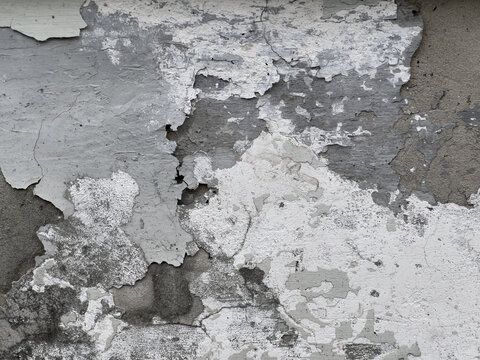Weathered exterior concrete wall with peeling paint and crumbling plaster revealing grey and white flake