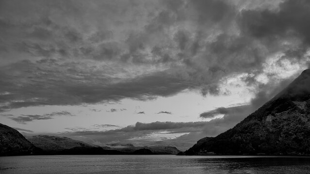 Dramatic Fjord Landscape Under Cloudy Sky in Black and White.