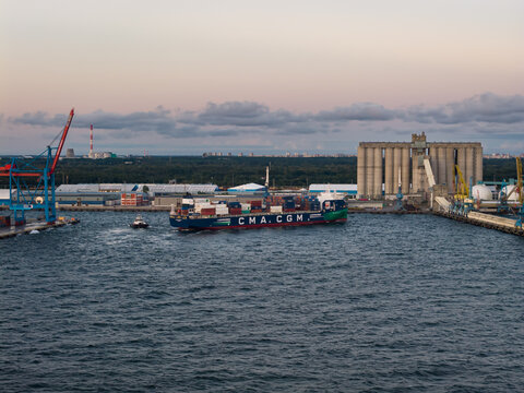 Muuga, Estonia - September 11, 2026: Aerial view of a CMA CGM container ship arriving at Muuga Harbour port with cranes, grain silos, and industrial infrastructure during dusk.