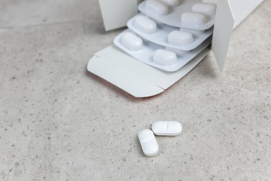 White tablets and blister packs on concrete surface with medical and healthcare concept.