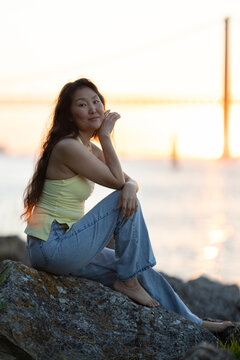 Asian woman relaxing on rocks during sunset