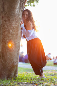 Woman smiling relaxing by tree trunk at sunset
