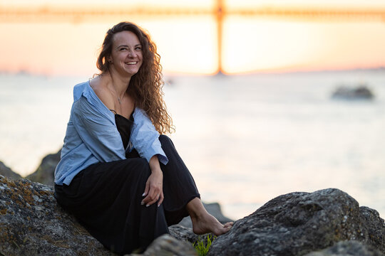 Woman smiling sitting on rocks enjoying sunset