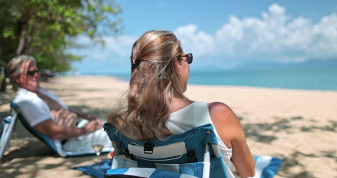 Mature couple relaxing on beach chairs under palm trees, enjoying a tropical vacation by the turquoise ocean, symbolizing leisure, travel, and serene retirement by the sea. Koh Samui Island, Thailand