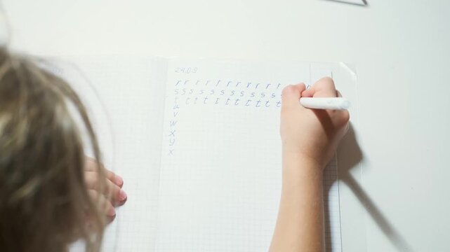 Child learns to write English alphabet letters, moving white pen across graph paper to practice repeated strokes while focused young student develops handwriting control and foundational literacy