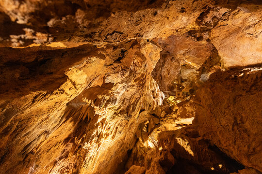 Lighting highlights rock formations in a cave with pathways for visitors in a natural underground setting
