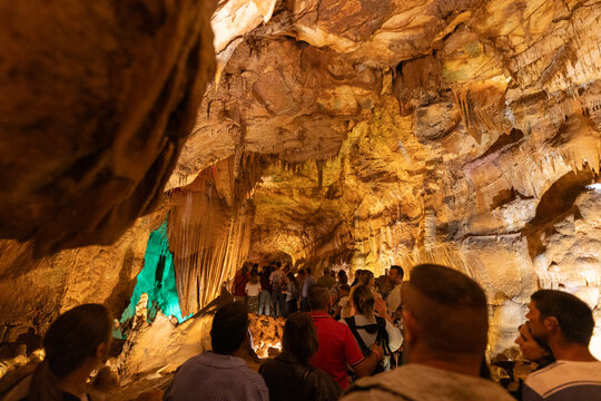 Visitors explore a cave with rock formations and colorful lights in the background during a guided tour