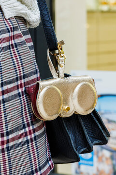Gros plan d&rsquo;un accessoire dor&eacute; fix&eacute; &agrave; la bandouli&egrave;re d&rsquo;un sac &agrave; main noir, port&eacute; avec une veste &agrave; carreaux.