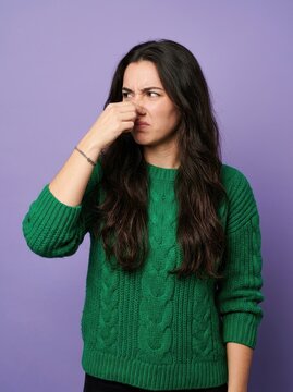 Young Woman Pinching Her Nose Due to Bad Smell Isolated on Purple Background