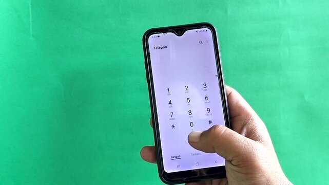 Close up of hand holding smartphone hesitant to press call button on green screen background, concept of communication uncertainty and anxiety.  