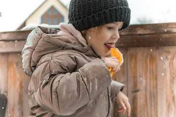 Playful little girl in a warm winter jacket eating clean snow from a toy shovel outdoors during winter vacation, candid childhood moment, playful emotion, and active cold season games © Katharina