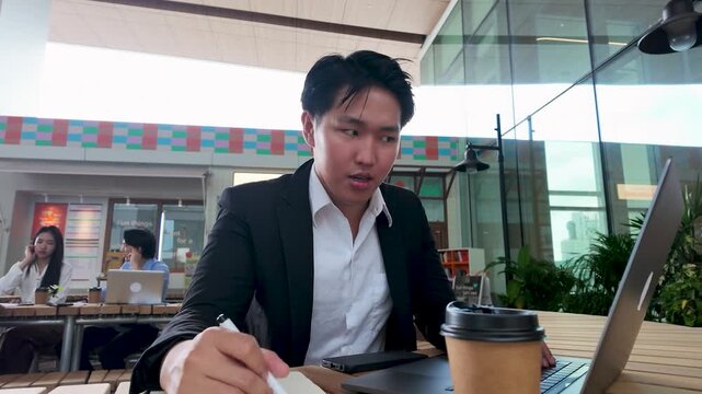 Confident Asian Businessman Working on Laptop in Modern Bangkok Cafe