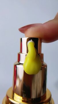Finger pressing the cap of a beauty product bottle, dispensing thick yellow cream liquid. Close up view, cosmetic skincare texture concept.