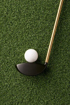 A top down view of a golf club and a white golf ball on a textured green artificial lawn.
