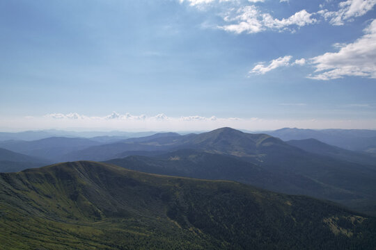 Panoramic view of rolling green mountain ranges and peaks under blue summer sky with white clouds