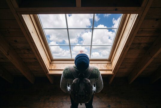 Person from behind looking up through skylight to sky above, overhead composition