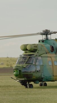 Vertical Screen: A combat helicopter lifts off the ground at an airport during an air show. The aircraft is preparing for a flight demonstration. Spectators watch the action.