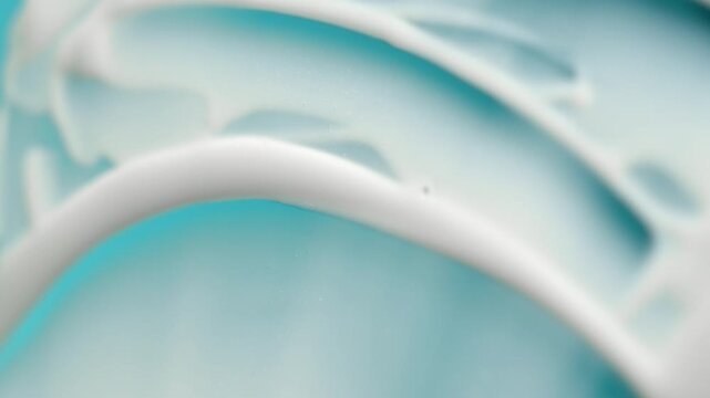 Smearing cosmetic white cream, lotion, or gel texture on a light blue background creating a wavy pattern with a spatula