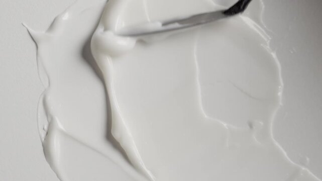 Cosmetic cream smearing with spatula on white background. Macro shot of white beauty product texture and skincare swatch