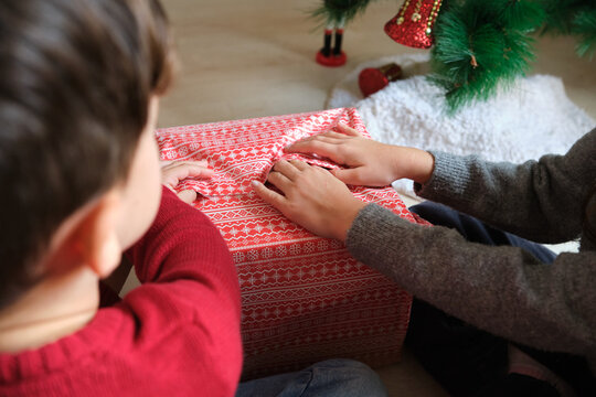 Children eagerly opening red christmas present together