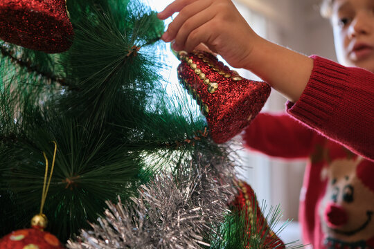 Child's hand hanging red christmas ornament on tree