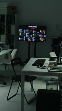 Vertical shot of empty scam office space showing glowing monitors with cyber data and financial statistics during night. Ideal for technology crime documentaries and cybersecurity presentations
