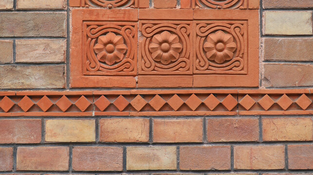 Ancient red brick wall texture. Historical building facade with decorative terracotta tiles and relief floral rosette pattern background.