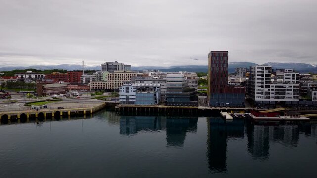 Modern city waterfront buildings reflecting in calm harbor water in Bodo, Norway. Aerial drone view