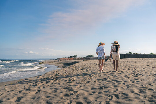 Senior and young woman walking barefoot on a beach with copy space
