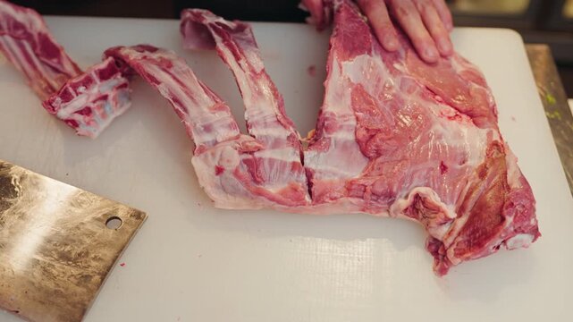 A chef separates ribs with a heavy cleaver on a cutting board in a professional kitchen.