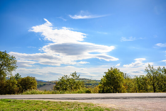 Rural road beneath lenticular clouds and rolling hills in the Montefeltro region of Marche, Italy