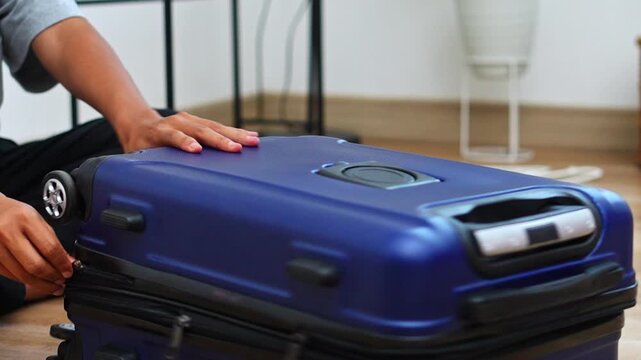 Traveler closing open blue travel suitcase on wooden floor at home