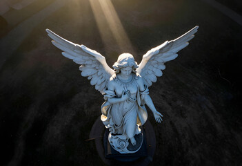 Fototapeta premium Spirituality and hope, marble angel statue with wings spread under divine light rays in a cemetery at sunset for religious and memorial concepts