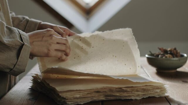 Placing hands in cuff, lifting-turning deckled sheets at skylight checking feel, ceramic bowl