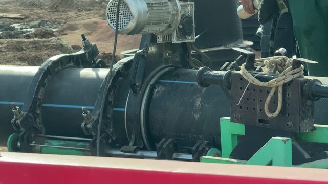 Industrial pipe welding equipment fusing black plastic polyethylene sections on construction site. Static shot focusing on heavy machinery engineering process detail.