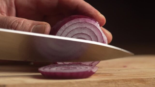Chef slicing red fresh raw onion on wooden board with sharp knife