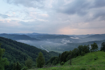 Fototapeta premium Scenic drone panorama of winding mountain river in green valley surrounded by forested slopes and morning fog
