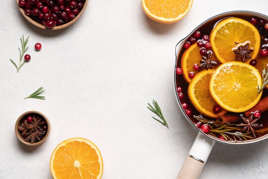 Hot mulled wine with cranberries, orange, rosemary, cinnamon and spices in a pot, Christmas winter drink on a light background with copy space