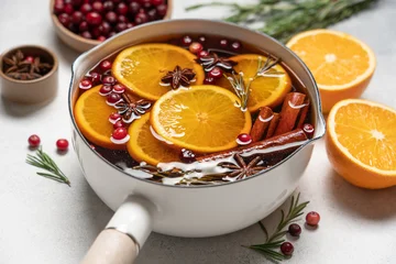 Hot mulled wine with cranberries, orange, rosemary, cinnamon and spices in a pot, Christmas winter drink on a light background with copy space © Anna Puzatykh
