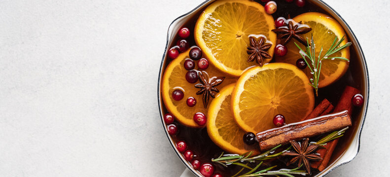 Hot mulled wine with cranberries, orange, rosemary, cinnamon and spices in a pot, Christmas winter drink on a light background with copy space