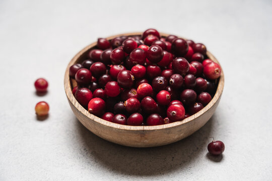 Fresh ripe cranberries in a wooden bowl on a light background, healthy seasonal autumn berries and harvest food