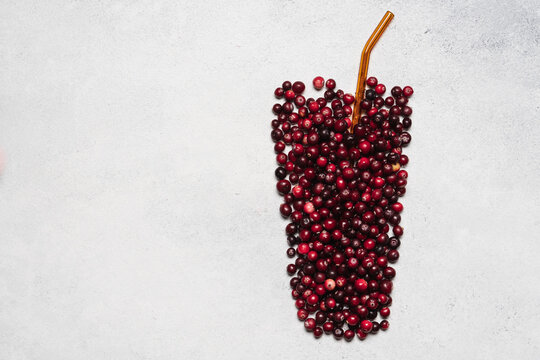 Fresh cranberries shaped like a glass with a straw on a light background, creative autumn food concept with copy space